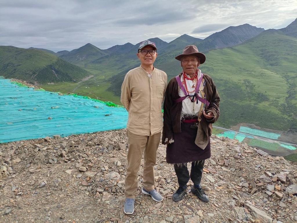 A visitor standing with a villager from Xinlong, with steep green hills behind them